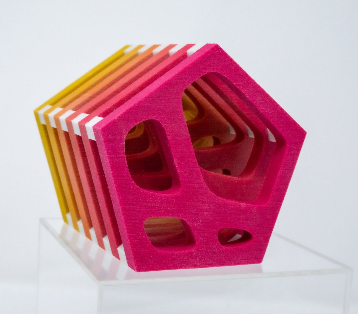 A Window Evolution sculpture: a stack of pentagonal slices shading from yellow to magenta, each with windows cut through it that change shape from slice to slice
