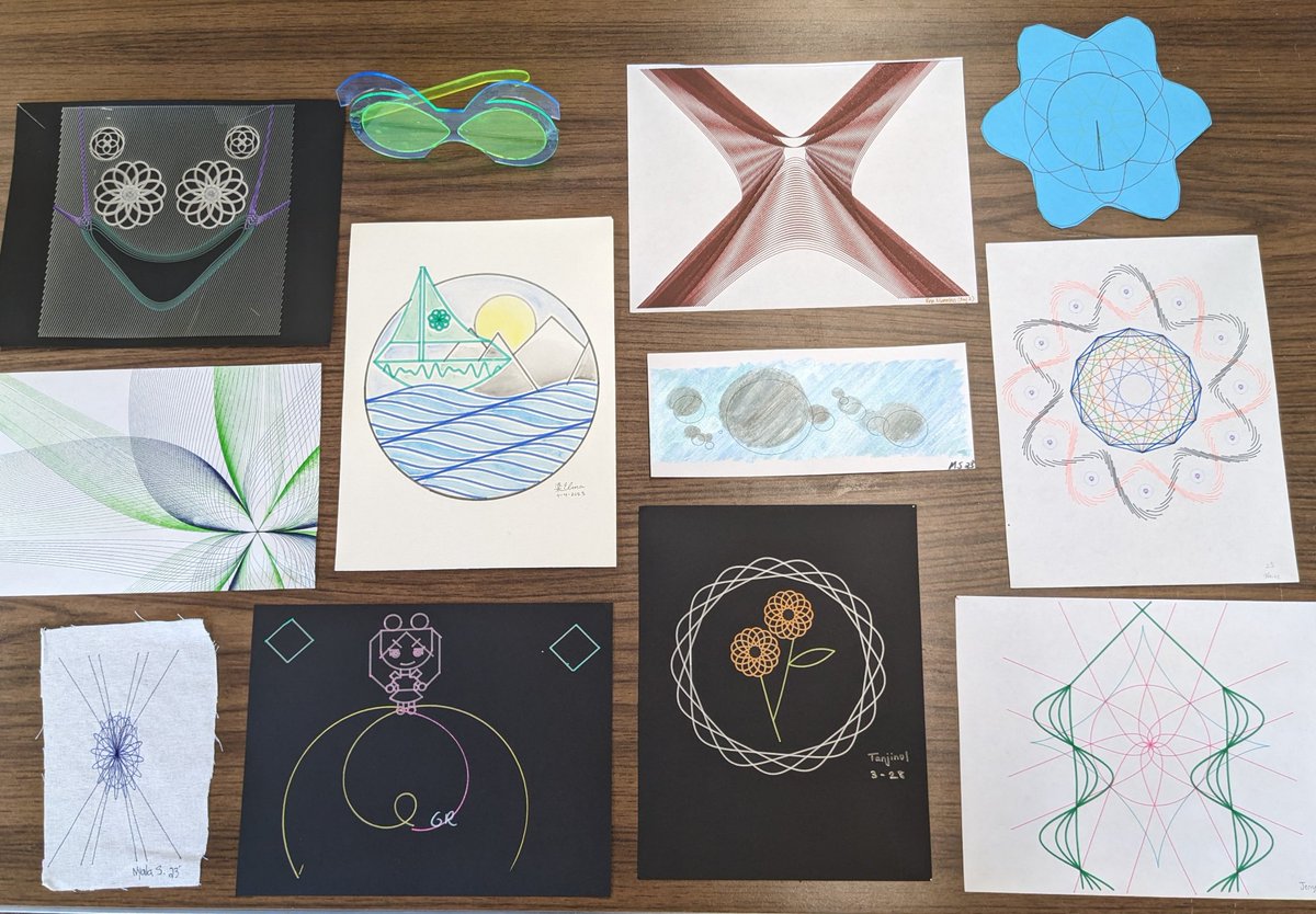 A table covered with a dozen pieces of student artwork drawn by a pen plotter, including string-art curves, spirographs, a sailboat, and a pair of laser-cut glasses